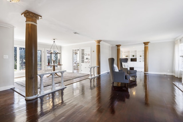 living room with dark wood-type flooring, crown molding, built in features, ornate columns, and a chandelier