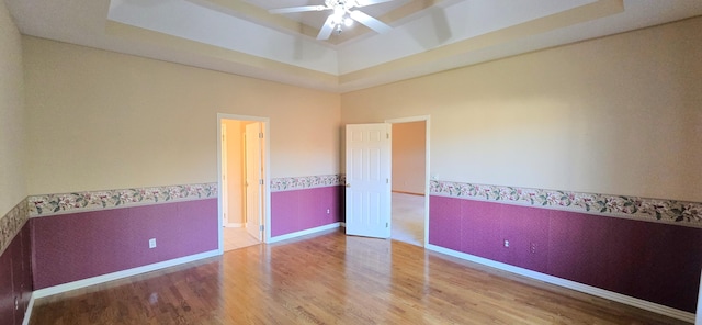 unfurnished bedroom featuring hardwood / wood-style floors, ceiling fan, and a tray ceiling