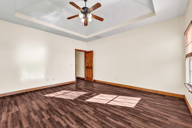 unfurnished room with ceiling fan, dark hardwood / wood-style flooring, and a tray ceiling