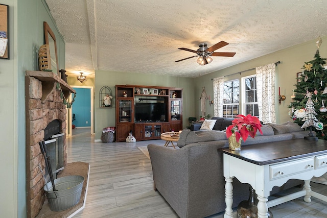 living room featuring ceiling fan, light hardwood / wood-style floors, a textured ceiling, and a fireplace