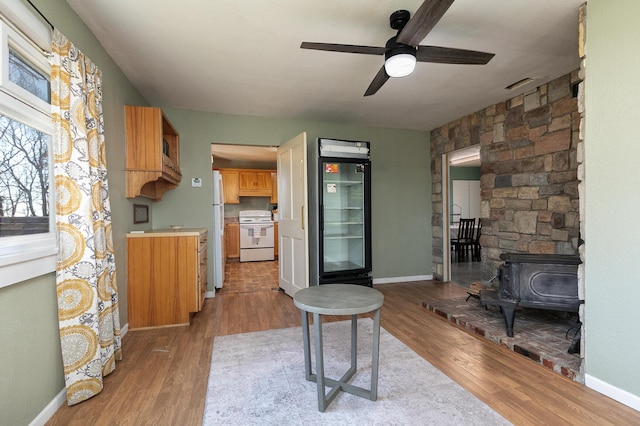 kitchen with ceiling fan, white appliances, a wood stove, and light wood-type flooring