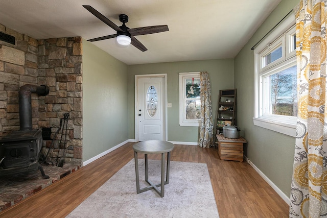 foyer entrance with ceiling fan, wood-type flooring, and a wood stove