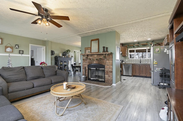 living room with a textured ceiling, ceiling fan, sink, light hardwood / wood-style flooring, and a stone fireplace