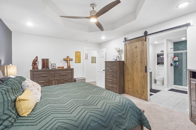 bedroom featuring ensuite bathroom, ceiling fan, a barn door, a tray ceiling, and light colored carpet