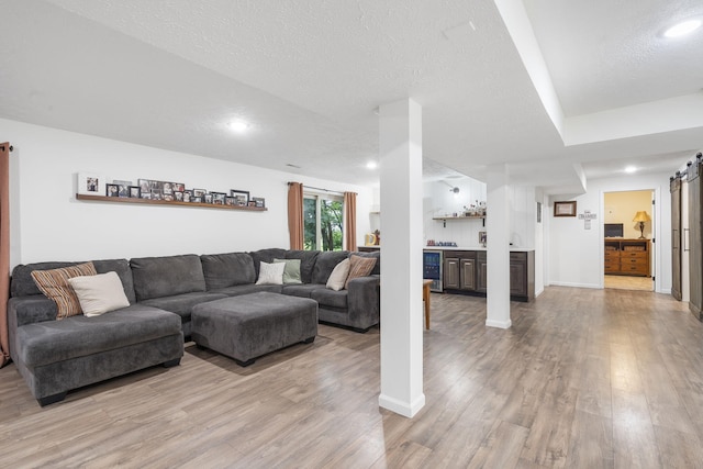 living room with wine cooler, a textured ceiling, light hardwood / wood-style flooring, and a barn door