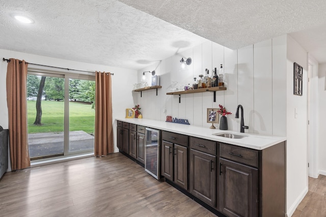 kitchen with sink, wine cooler, dark brown cabinetry, a textured ceiling, and wood-type flooring