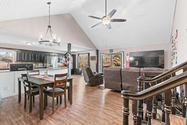 dining area featuring ceiling fan with notable chandelier, light hardwood / wood-style floors, and high vaulted ceiling