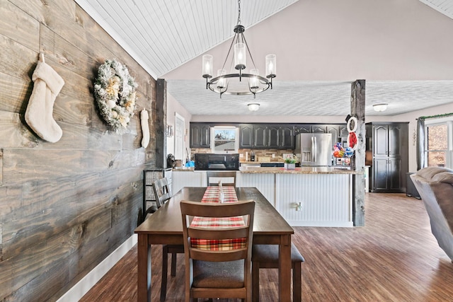 dining area featuring wooden walls, hardwood / wood-style flooring, lofted ceiling, and a notable chandelier