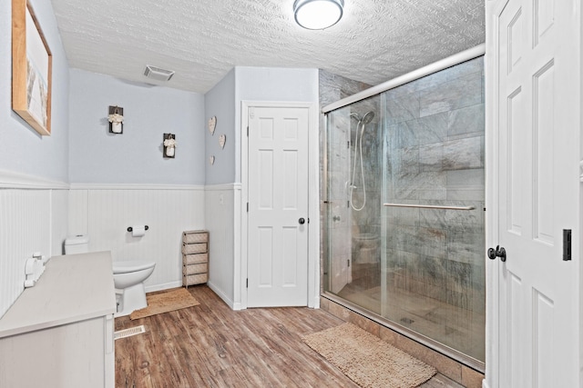 bathroom featuring a textured ceiling, hardwood / wood-style flooring, toilet, and an enclosed shower