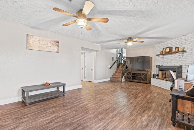 living room featuring hardwood / wood-style floors, a textured ceiling, a brick fireplace, and ceiling fan