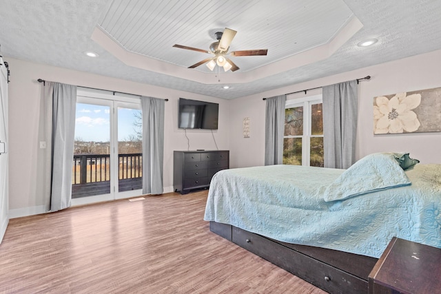 bedroom with hardwood / wood-style floors, access to outside, a raised ceiling, ceiling fan, and a textured ceiling