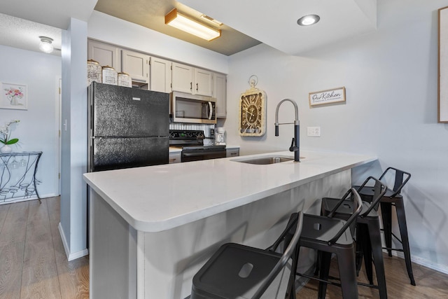 kitchen with black appliances, a breakfast bar, light hardwood / wood-style floors, and sink