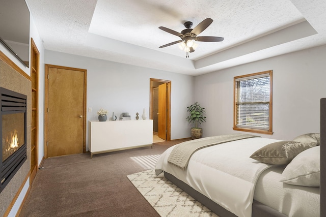 carpeted bedroom featuring a raised ceiling, ceiling fan, and a textured ceiling