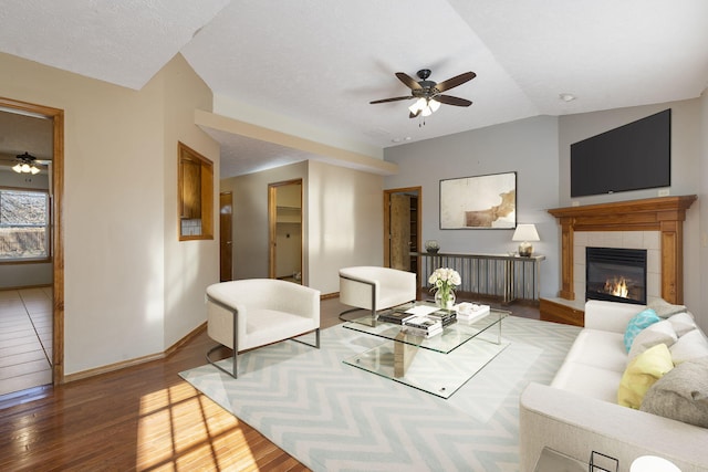 living room featuring a textured ceiling, ceiling fan, hardwood / wood-style flooring, a fireplace, and lofted ceiling