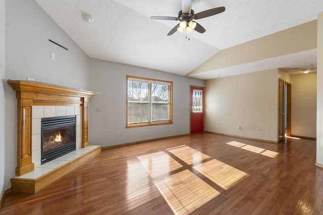 unfurnished living room with a textured ceiling, a tiled fireplace, lofted ceiling, and light wood-type flooring