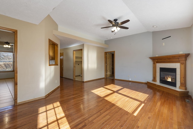 unfurnished living room featuring a textured ceiling, vaulted ceiling, ceiling fan, hardwood / wood-style floors, and a tiled fireplace