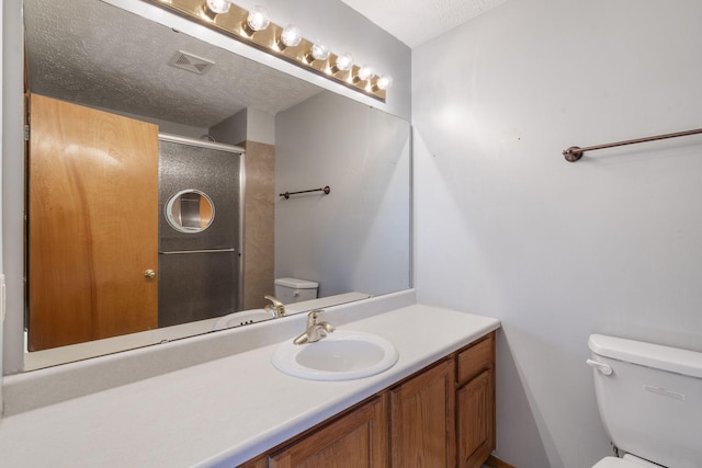 bathroom with a shower with door, vanity, a textured ceiling, and toilet