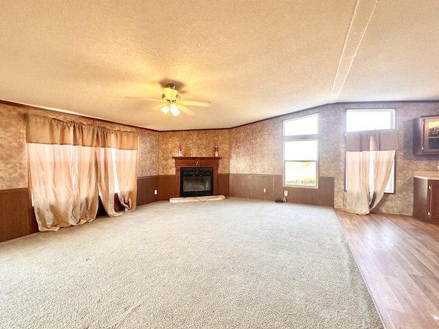 unfurnished living room with hardwood / wood-style floors, wood walls, lofted ceiling, ceiling fan, and a textured ceiling