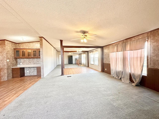 unfurnished living room with a textured ceiling, ceiling fan, wooden walls, light hardwood / wood-style floors, and lofted ceiling