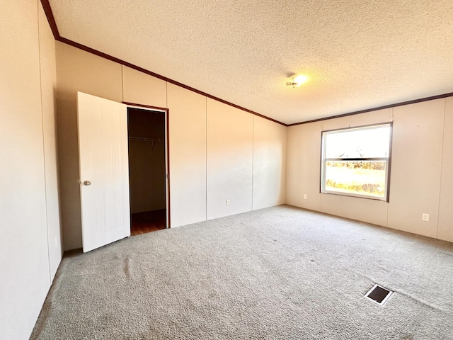 unfurnished bedroom featuring a textured ceiling, carpet floors, a spacious closet, and crown molding