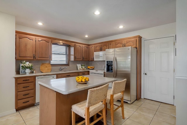 kitchen featuring a center island, white appliances, decorative backsplash, light tile patterned floors, and a breakfast bar area