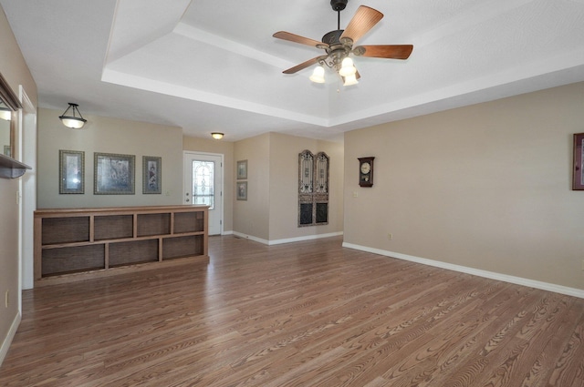 unfurnished living room featuring a tray ceiling, ceiling fan, and wood-type flooring