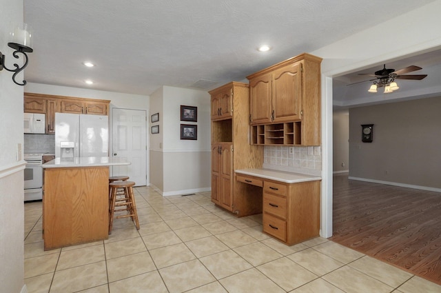 kitchen with a breakfast bar, a center island, white appliances, light hardwood / wood-style flooring, and decorative backsplash