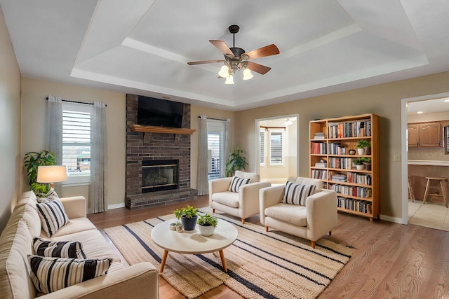 living room featuring a fireplace, light hardwood / wood-style flooring, a raised ceiling, and ceiling fan