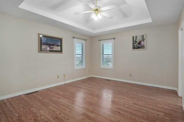 empty room with wood-type flooring, a tray ceiling, and ceiling fan