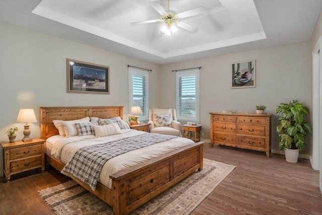 bedroom featuring ceiling fan, a raised ceiling, and dark wood-type flooring