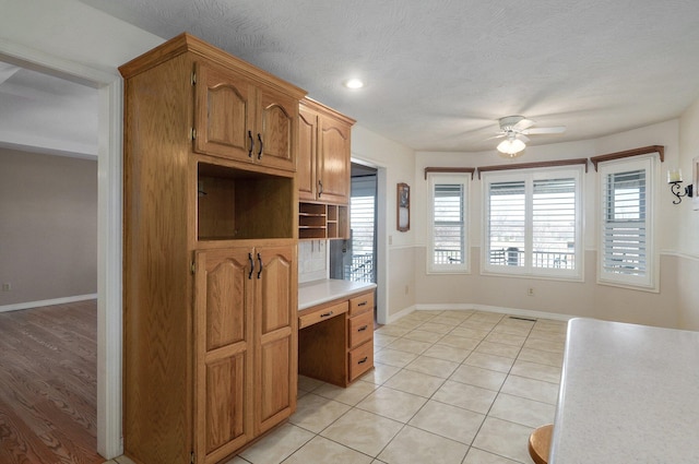 kitchen featuring ceiling fan, light tile patterned flooring, built in desk, and a textured ceiling