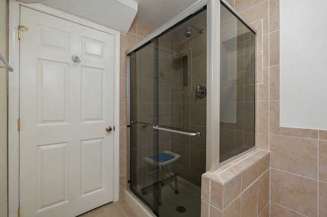 bathroom featuring a textured ceiling, an enclosed shower, and tile walls