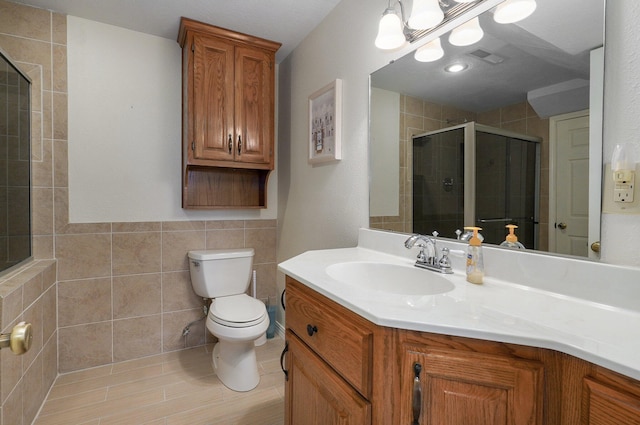 bathroom featuring vanity, toilet, an enclosed shower, and tile walls