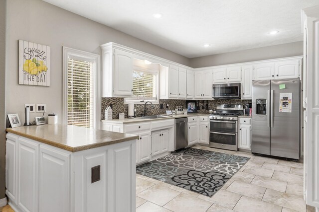 kitchen with kitchen peninsula, appliances with stainless steel finishes, backsplash, sink, and white cabinetry