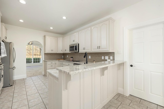 kitchen featuring kitchen peninsula, appliances with stainless steel finishes, light stone countertops, tasteful backsplash, and white cabinets