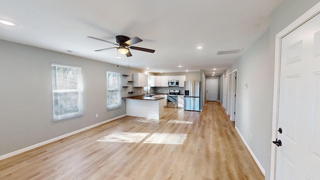 kitchen with kitchen peninsula, appliances with stainless steel finishes, ceiling fan, light hardwood / wood-style flooring, and white cabinetry