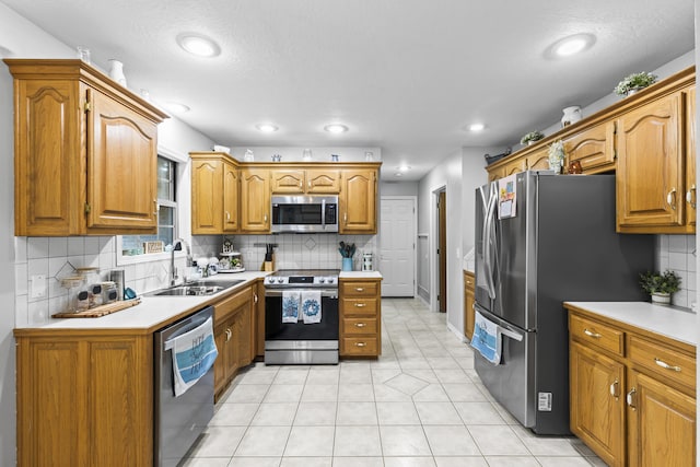 kitchen featuring sink, a textured ceiling, decorative backsplash, light tile patterned flooring, and appliances with stainless steel finishes