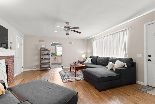 living room with ceiling fan, light wood-type flooring, and a fireplace