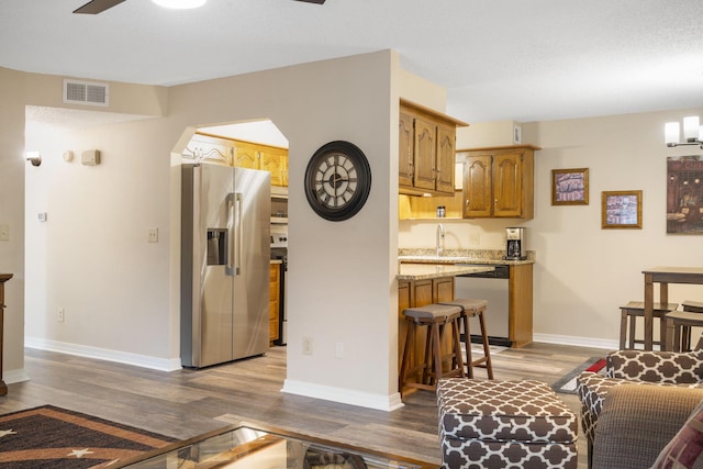 kitchen featuring ceiling fan, sink, light stone counters, wood-type flooring, and appliances with stainless steel finishes