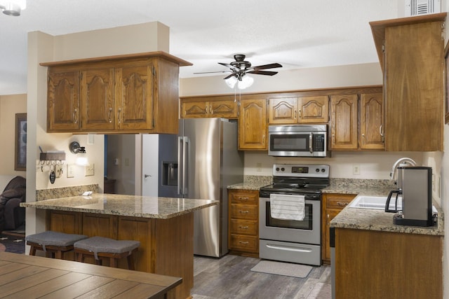 kitchen featuring a kitchen breakfast bar, sink, dark hardwood / wood-style floors, appliances with stainless steel finishes, and light stone counters