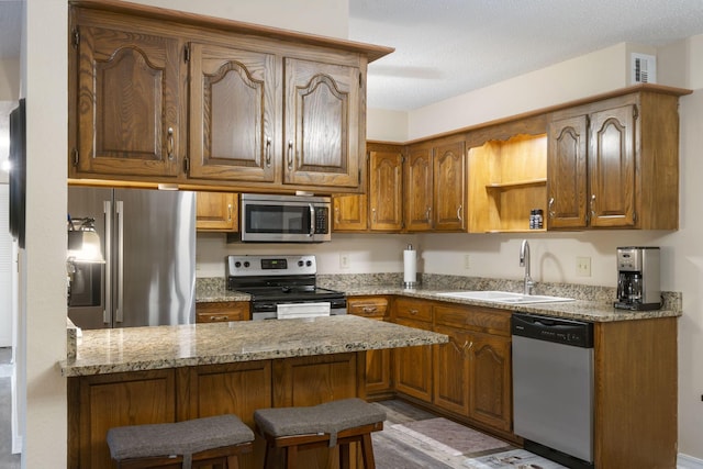 kitchen featuring sink, a kitchen breakfast bar, light stone counters, kitchen peninsula, and appliances with stainless steel finishes