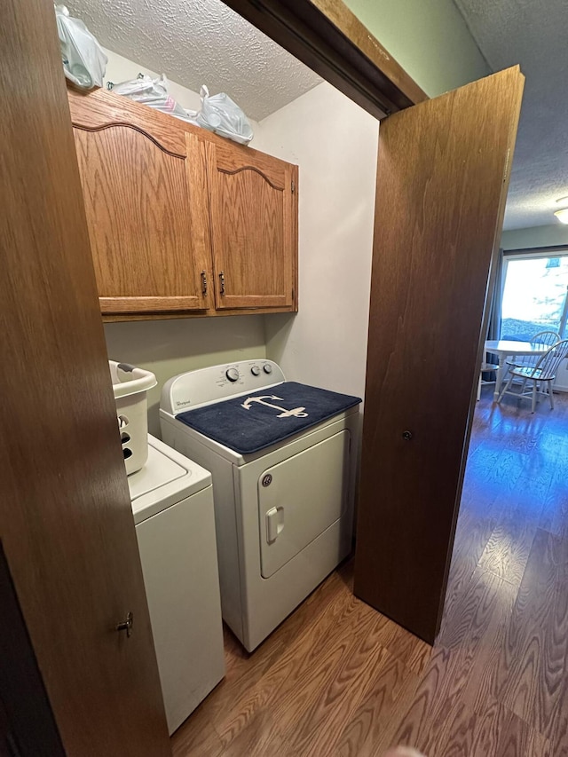 laundry area with cabinets, washing machine and dryer, a textured ceiling, and light hardwood / wood-style flooring