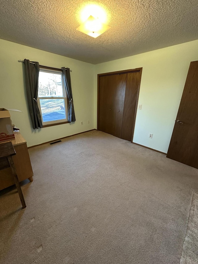 unfurnished bedroom featuring a textured ceiling, light colored carpet, and a closet