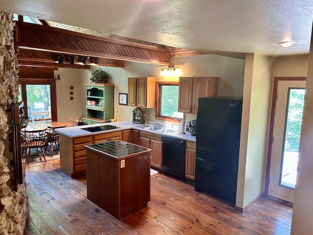 kitchen with kitchen peninsula, a kitchen island, black appliances, and dark hardwood / wood-style floors