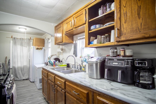 kitchen with sink, crown molding, light stone countertops, stainless steel range oven, and light wood-type flooring