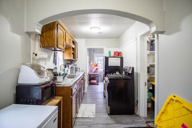 kitchen with hardwood / wood-style flooring, black refrigerator, washer / clothes dryer, and stainless steel gas stove