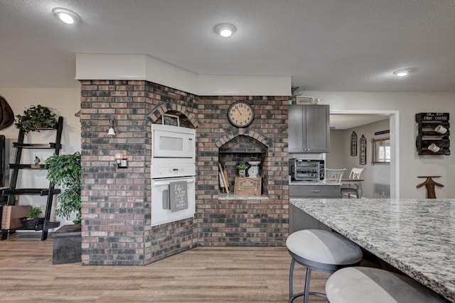 kitchen featuring a textured ceiling, white appliances, light hardwood / wood-style floors, and light stone counters