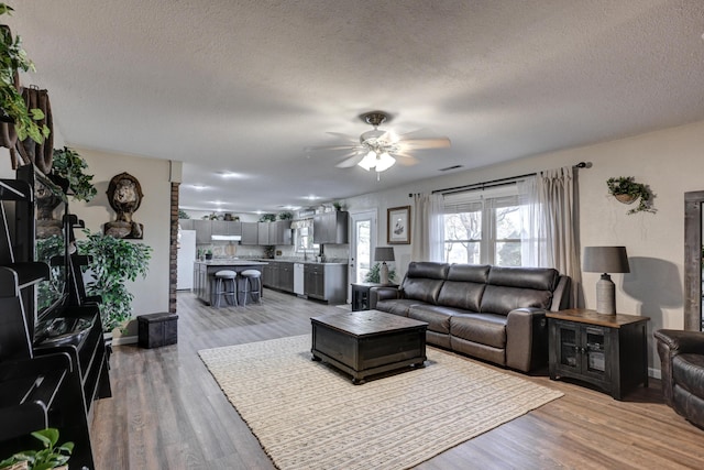 living room featuring ceiling fan, light hardwood / wood-style flooring, and a textured ceiling