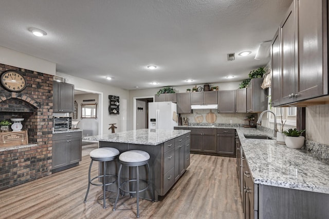 kitchen featuring white fridge with ice dispenser, a center island, sink, a breakfast bar area, and light wood-type flooring