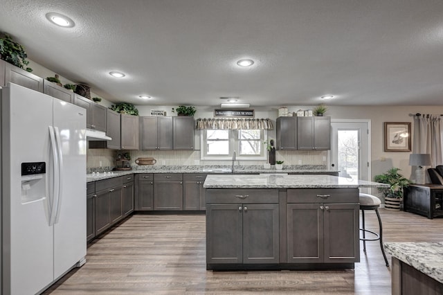 kitchen with white refrigerator with ice dispenser, a kitchen breakfast bar, light wood-type flooring, a textured ceiling, and light stone counters